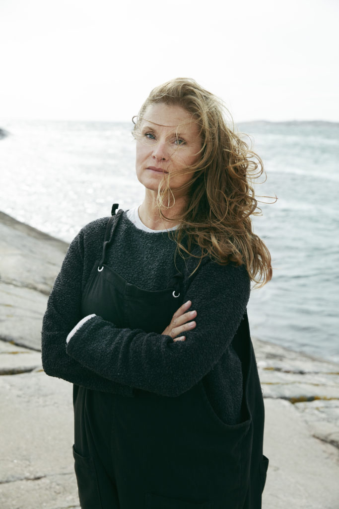 Kvinna står framför hav på en klippa. 