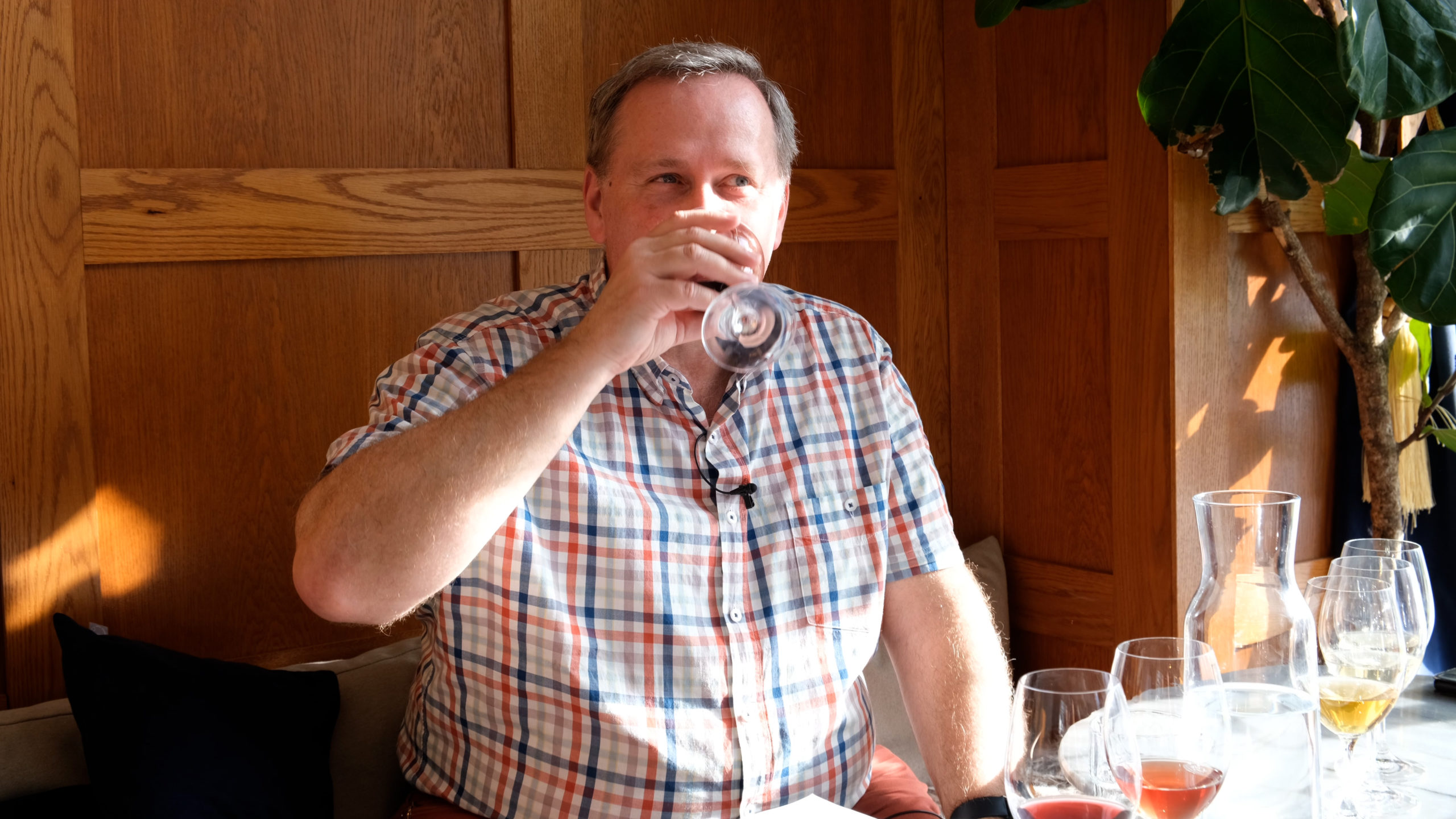 En medelåldersman sitter på et vincafe och dricker ett glas rött vin. Han bär en färgglad rutig piké.